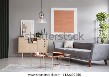 Modern couch and copper tables in a grey living room interior with a painting. Real photo