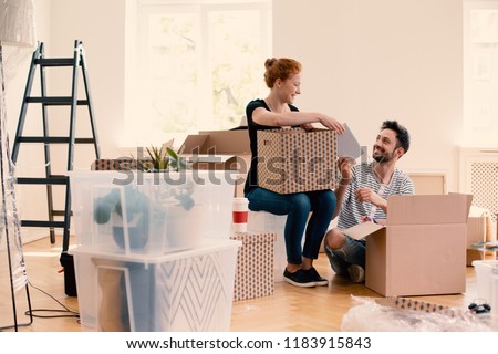 Happy man and woman unpacking stuff from cartoon boxes while furnishing interior