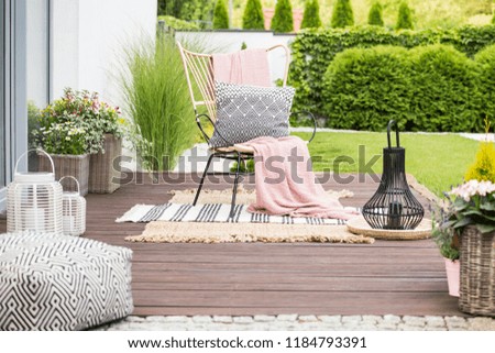 Real photo of a white pillow and pink blanket on a rattan chair standing in the garden of a luxurious house