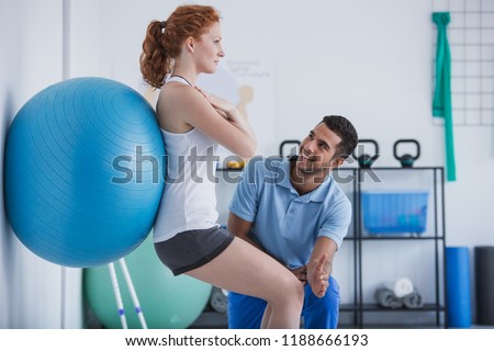 Smiling professional personal trainer helping sportswoman exercising with ball