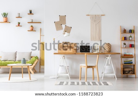 Real photo of a natural home office interior desk organizer, macrame on a wall, shelves and couch