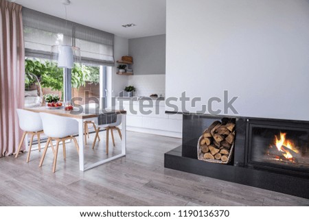 Real photo of a fireplace in a modern kitchen and dining room interior. Empty wall, place for your painting