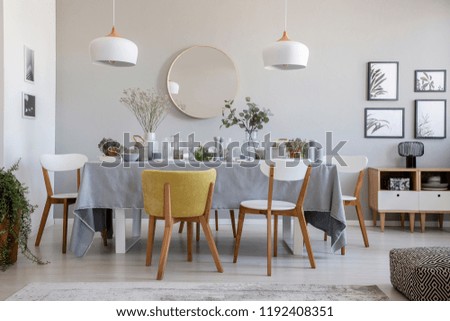 Real photo of an elegant dining room interior with a laid table, chairs, mirror on a wall and lamps