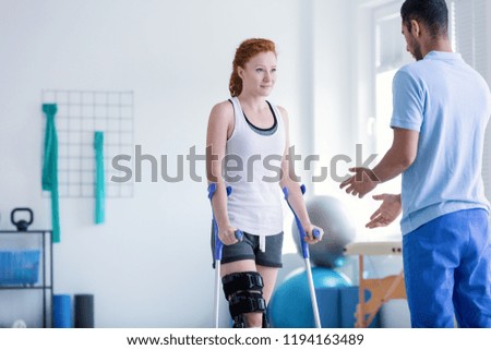 Woman with crutches during rehabilitation with helpful physiotherapist