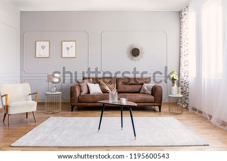 Minimal interior design of living room with brown leather couch, retro armchair coffee table and golden decorations, real photo