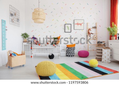 Poufs on colorful rug in scandi baby\'s bedroom interior with lamp, cradle and posters. Real photo