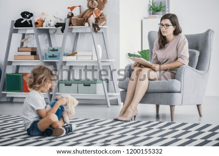 A diagnostics session of a child with development and social problems. Young professional social worker observing a kid sitting on a floor.