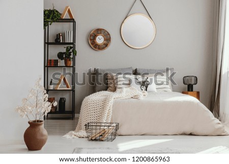 Round mirror and clock above bed with pillows in bright bedroom interior with flowers. Real photo