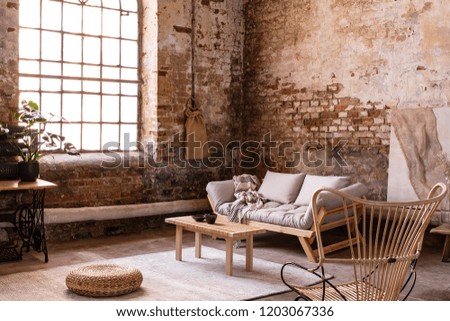 Pouf and wooden table on carpet near window in bright wabi sabi interior with sofa and armchair. Real photo