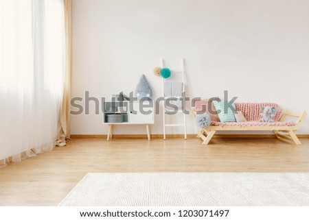Scandi child room interior in real photo with carpet on the floor, window with drapes, cupboard with raindrop cushion and lounge with blanket and pompom