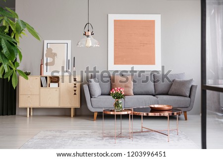 Large painting on a gray wall above an elegant sofa with cushions in a stylish living room interior with copper furniture