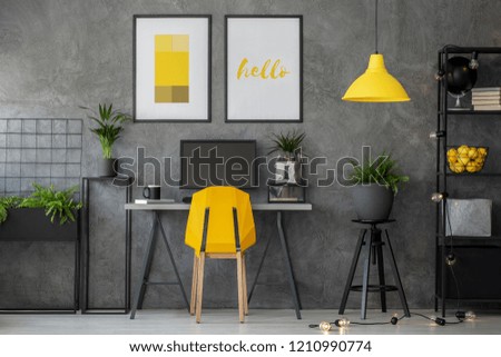 Stylish yellow and grey home office with industrial furniture and urban jungle, real photo with posters on concrete wall