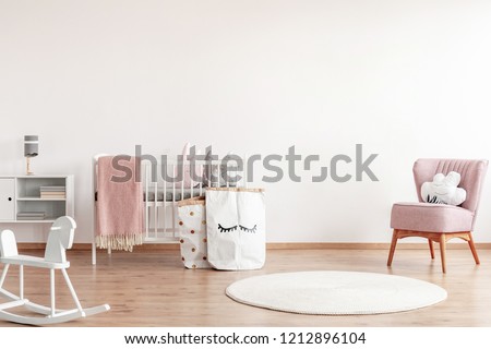 Bright scandinavian baby room with rocking horse, white nursery and pink armchairs, posters on the wall