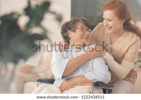 Smiling nurse supporting happy disabled elderly woman in the wheelchair