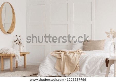 White simple bedroom design with mirror, dresser and comfortable bed with white sheets, real photo