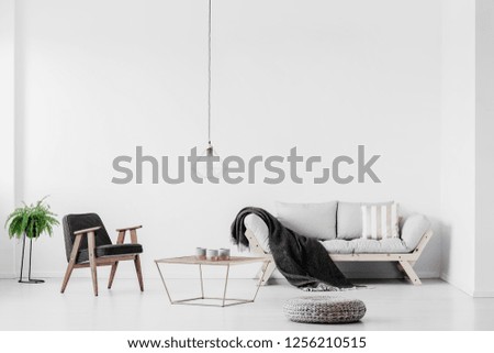 Stylish grey armchair next to industrial coffee table with candles in bright living room interior with scandinavian settee
