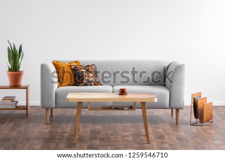 Wooden coffee table in the middle of elegant living room with grey couch and magazine rack on the wooden floor, real photo