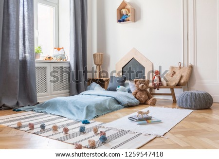 Pouf, rugs and plush toy in bright child\'s bedroom interior with window and blue bed. Real photo