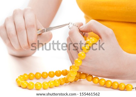 Girl\'s hands making a yellow necklace with a pliers