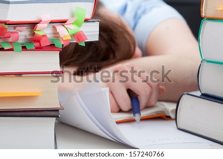 Overworked student sleeping on desk around the piles of books