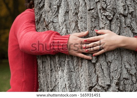 Happy couple surrounding tree trunk by arms in park