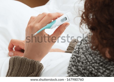 Sick woman with cold checking an electronic thermometer