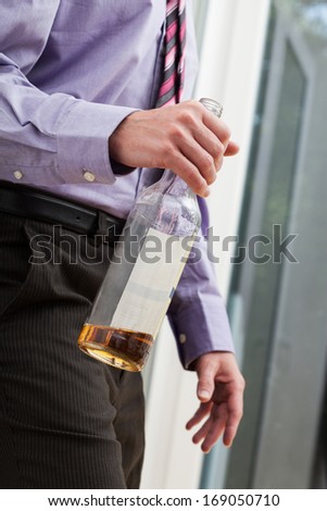 Drunk businessman wearing a tie, walking with the bottle in his hands