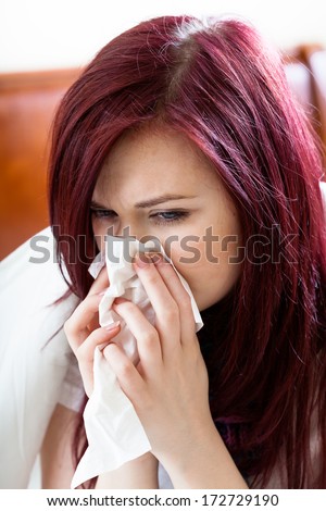 Woman sitting on her bed and blowing nose