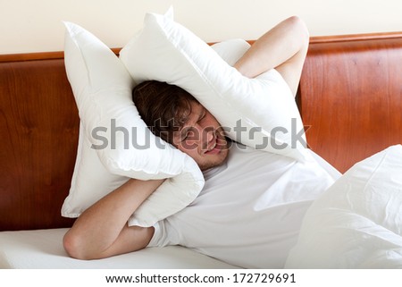 Man covering ears by pillows because of noise
