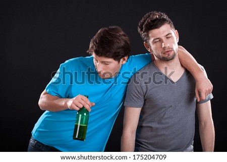 Two men friends standing drunk with a bottle of beer