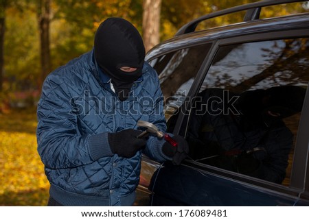 A masked criminal about to steal a car