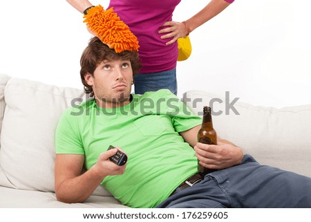 Man is drinking beer and watching tv while his wife cleaning house