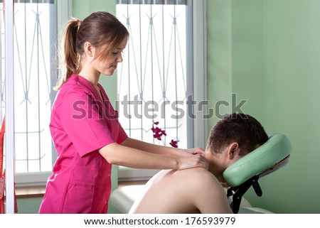 Pretty physiotherapist in rose apron doing back massage