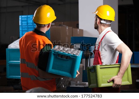 Two factory workers holding boxes with equipment during work