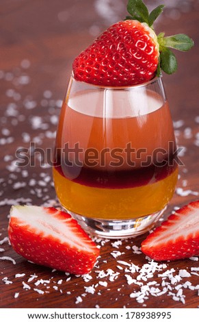 Layered fruit drink surrounded by coconut flakes and strawberries