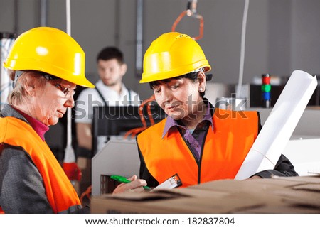 Two female workers in yellow safety helmets in factory