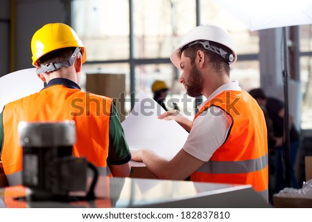 Male factory worker and supervisor are analyzing plans