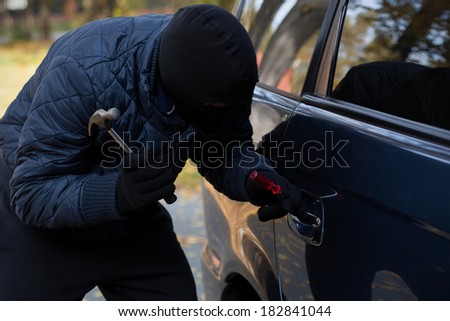 A masked burglar trying to break in a car using a hammer