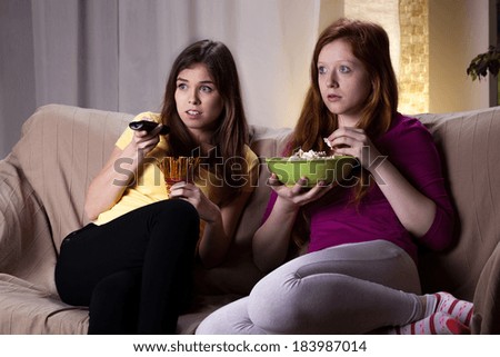 Young girls watching scary movie and eating popcorn