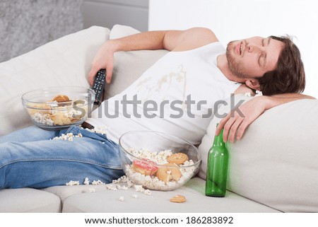 Alcoholic sleeping on couch among beer and sweets