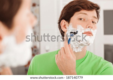 Handsome man shaving before the mirror in bathroom