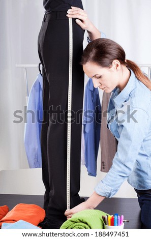 Young female tailor measuring black pant suit
