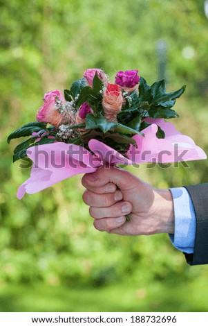 A man\'s hand with a bunch of pink roses