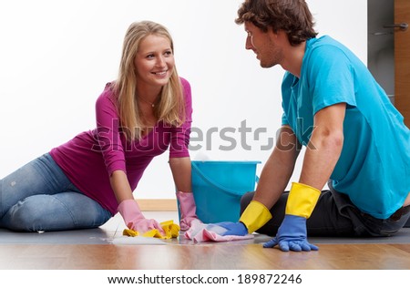 A couple cleaning the floor with dusters in gloves