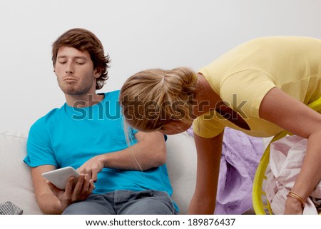A lazy man using a tablet and a woman cleaning up