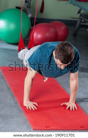 Young man exercising in suspension on gym mat