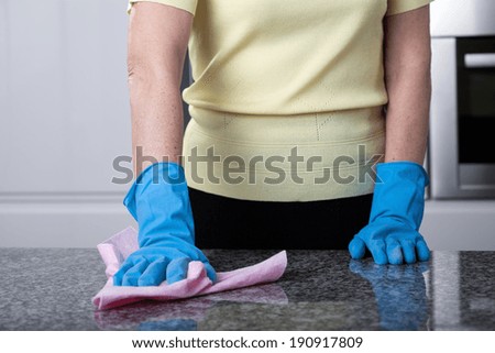 A closeup of a woman in gloves cleaning a kitchen top with a duster