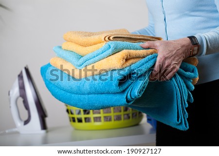 A closeup of a pile of towels, an iron and a basket in the background