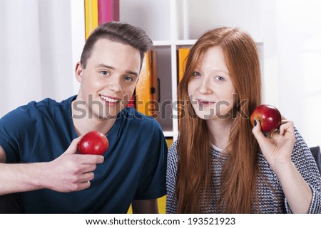 Happy male and female teenagers are holding apples