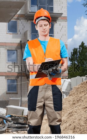 Engineer filling papers at building site, vertical